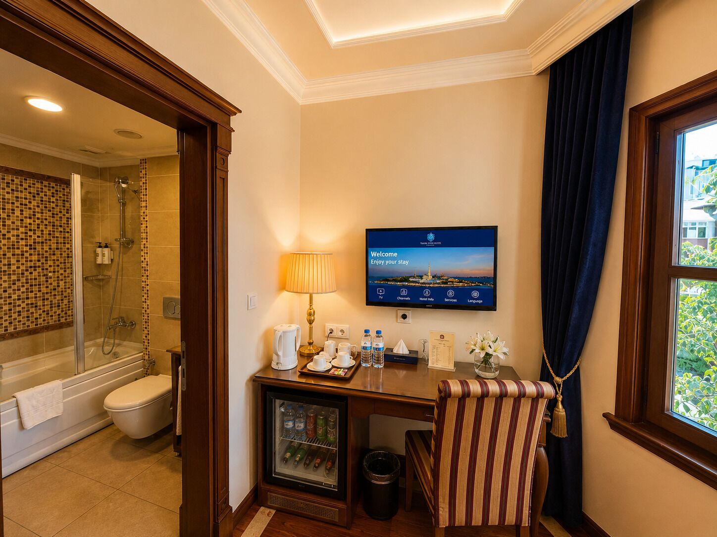 A hotel bathroom with a shower, toilet, and a TV mounted on the wall displaying a welcome message.
