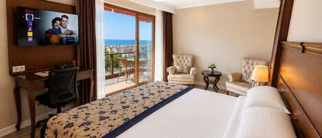 A hotel room with a bed, a desk, a TV, a balcony with a view, and two armchairs.