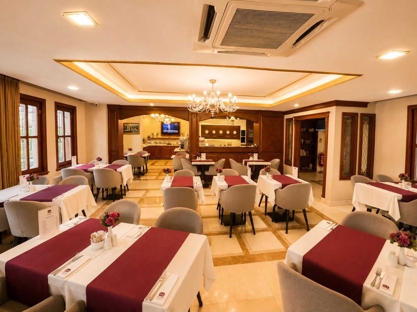 A hotel dining area with tables set for service, a bar in the background, and a chandelier.