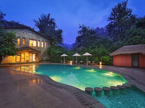 A swimming pool with lounge chairs and umbrellas, surrounded by trees and a stone building. - Corbett Gateway Resort & Spa (Ramnagar)