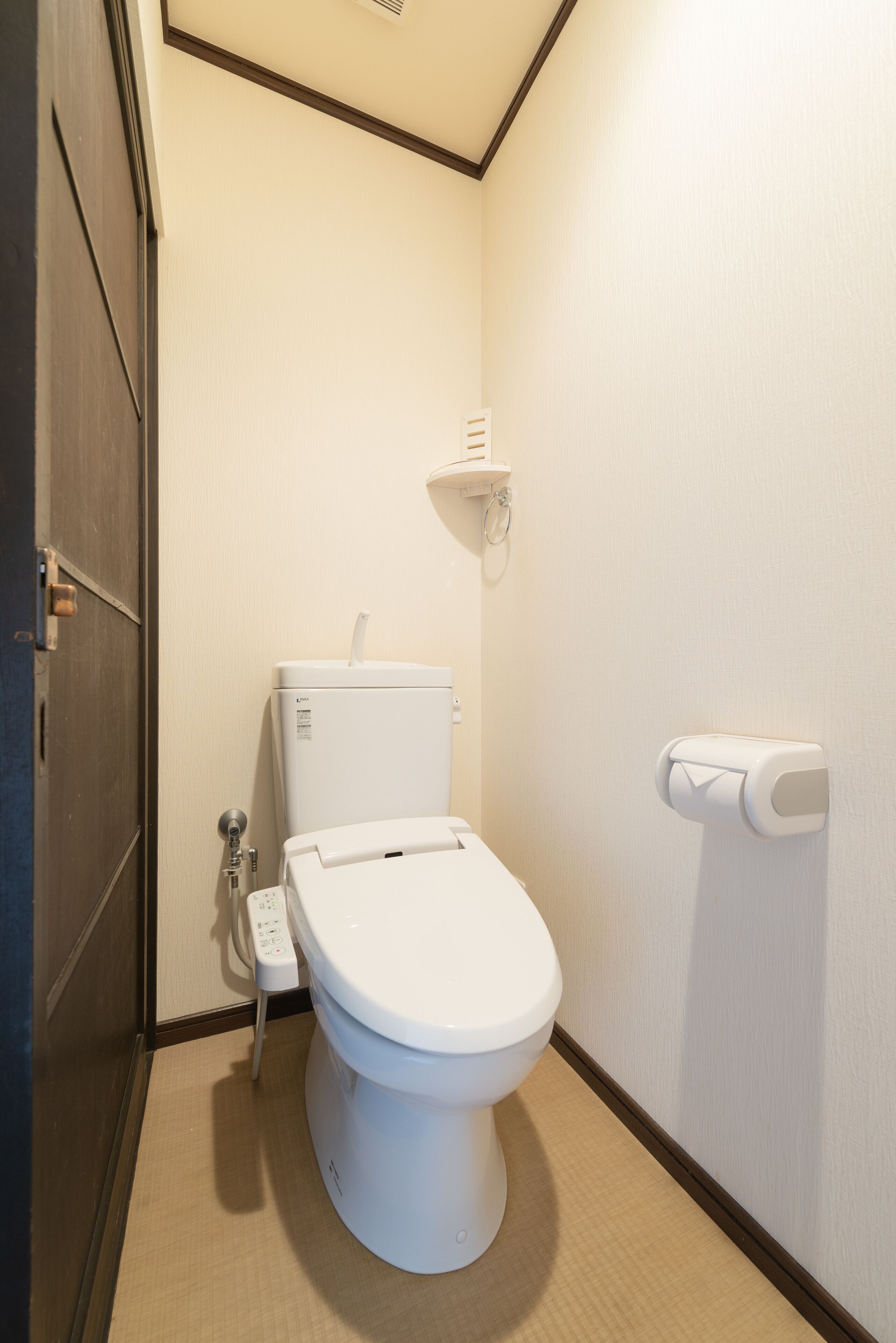 A small, clean bathroom with a toilet, a paper towel dispenser, and a toilet paper holder on the wall.