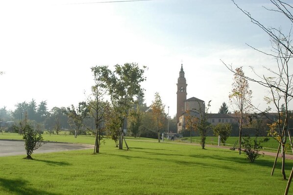 A grassy field with trees and a building with a tower in the background. - Hotel Conte Verde (Montecchio Emilia)