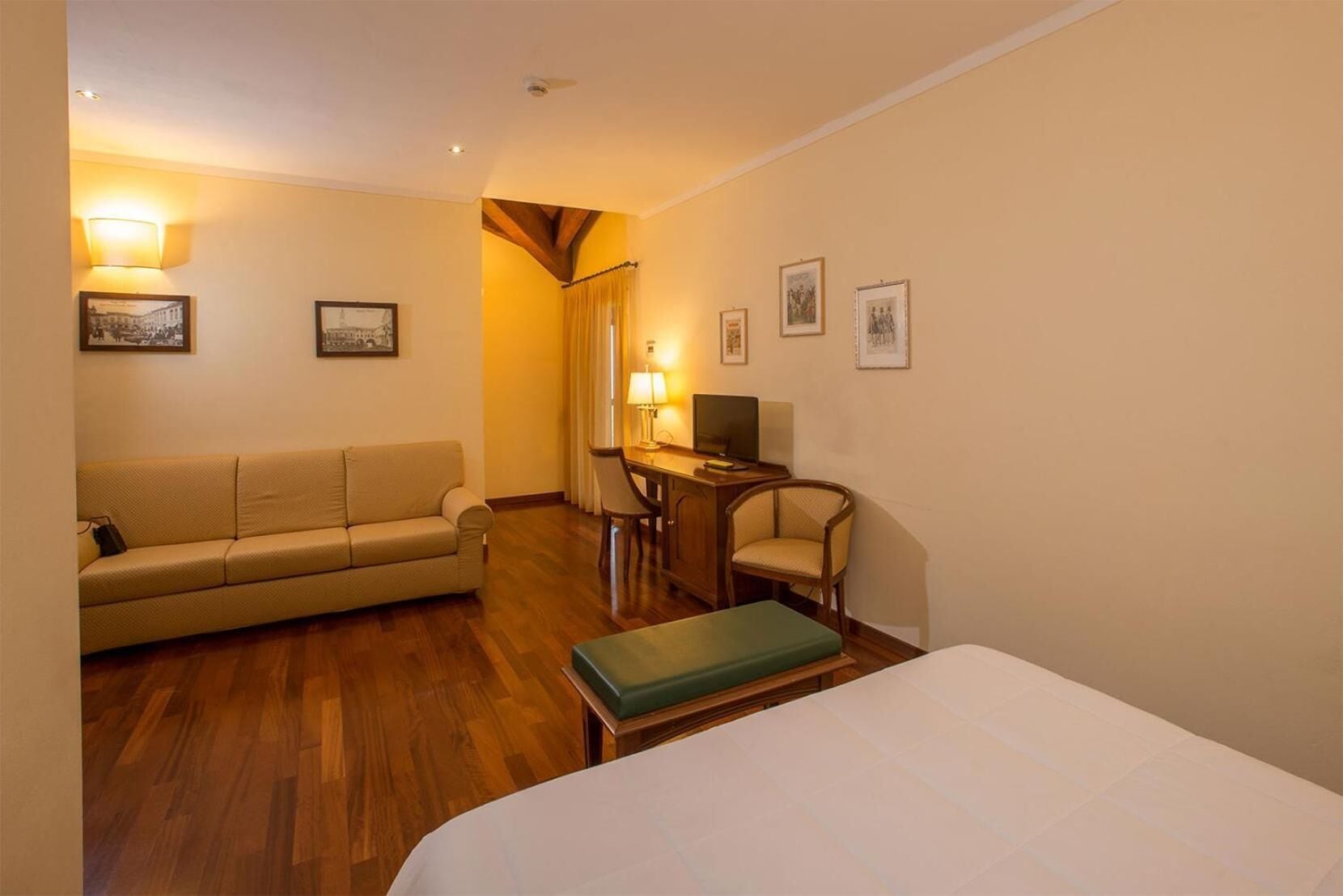 Habitación de hotel con cama, sofá, escritorio con silla y televisor.