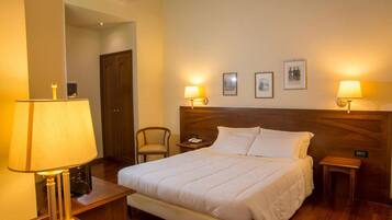 Una habitación de hotel con cama, lámparas de noche, una silla y cuadros en la pared.