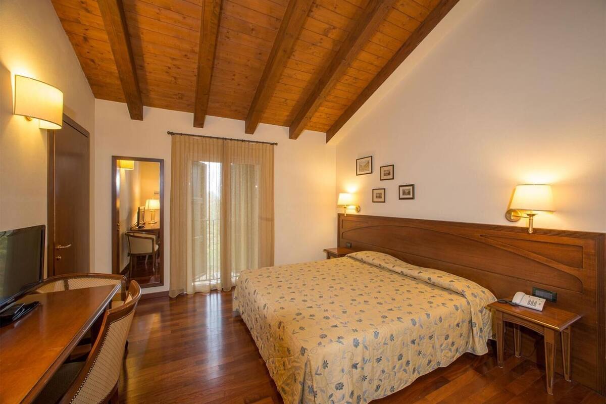 Ein Hotelzimmer mit Holzboden, einem Bett mit Blumenmuster-Bettwäsche, einem Schreibtisch mit Stuhl und einem Fernseher.