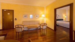 Habitación de hotel con sofá, dos sillones, una mesita, cama y puerta.