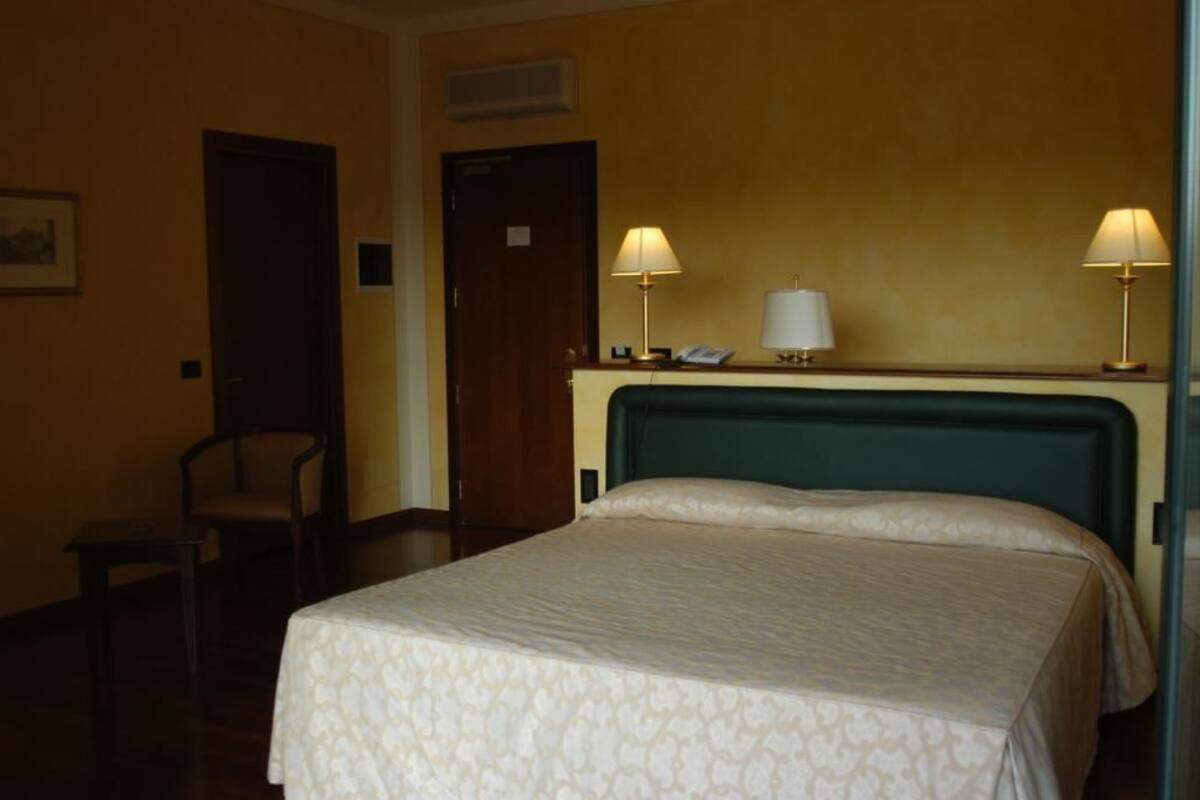 Ein Hotelzimmer mit einem Bett, zwei Nachttischlampen, einem Sessel, einem Schreibtisch und einer Tür.