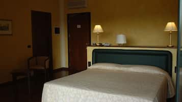 A hotel room with a bed, two bedside lamps, a chair, a desk, and a door.
