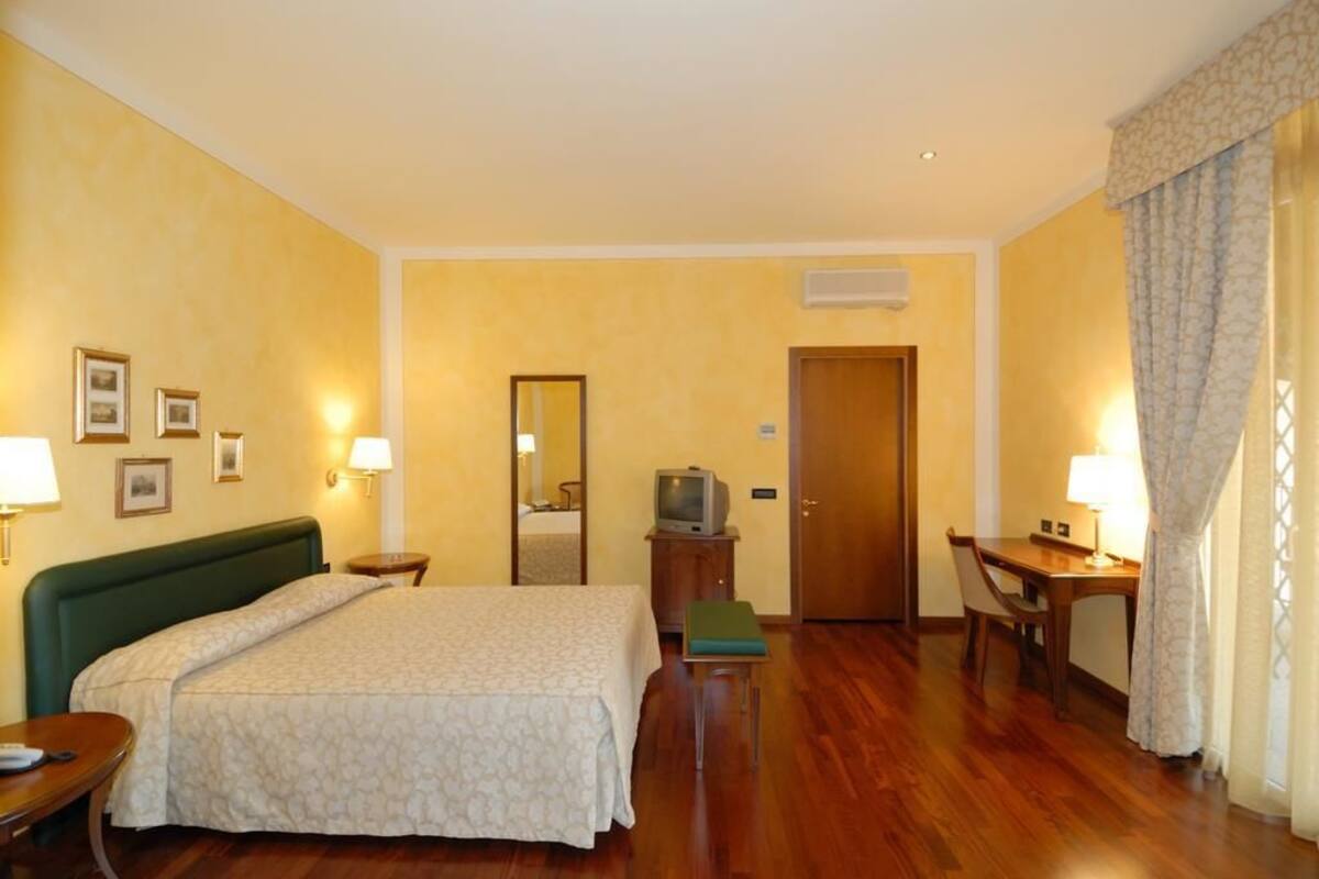 Ein Hotelzimmer mit Bett, Nachttischen, Schreibtisch, Fernseher und Spiegel.
