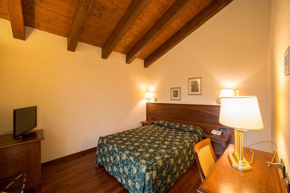 Ein Schlafzimmer mit einem Bett, einem Schreibtisch mit Lampe, einem Sessel und einem Fernseher auf einer Holzkommode.