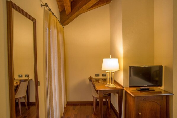A hotel room with a wooden desk, a lamp, a television, and a chair.