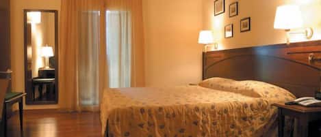 Un dormitorio con cama de madera, mesita de noche, silla, escritorio, espejo y ventana con cortinas.