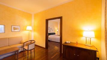 Ein Hotelzimmer mit Holzboden, einer Couch, einem Sessel, einem Schrank und einem Bett mit Kopfteil.