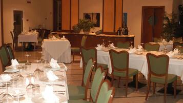 Un espace repas avec des tables dressées pour accueillir plusieurs convives, des chaises et un coin bar avec des bouteilles.