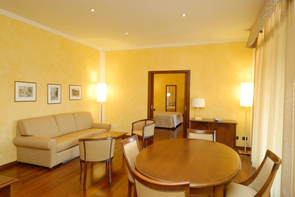 Habitación de hotel con sofá, mesa de comedor con sillas, escritorio con lámpara y cama.