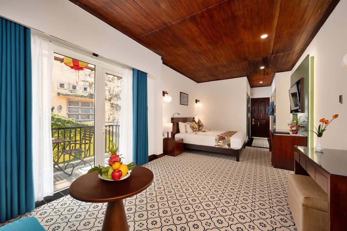 A hotel room with a balcony, a bed, a desk, and a TV.