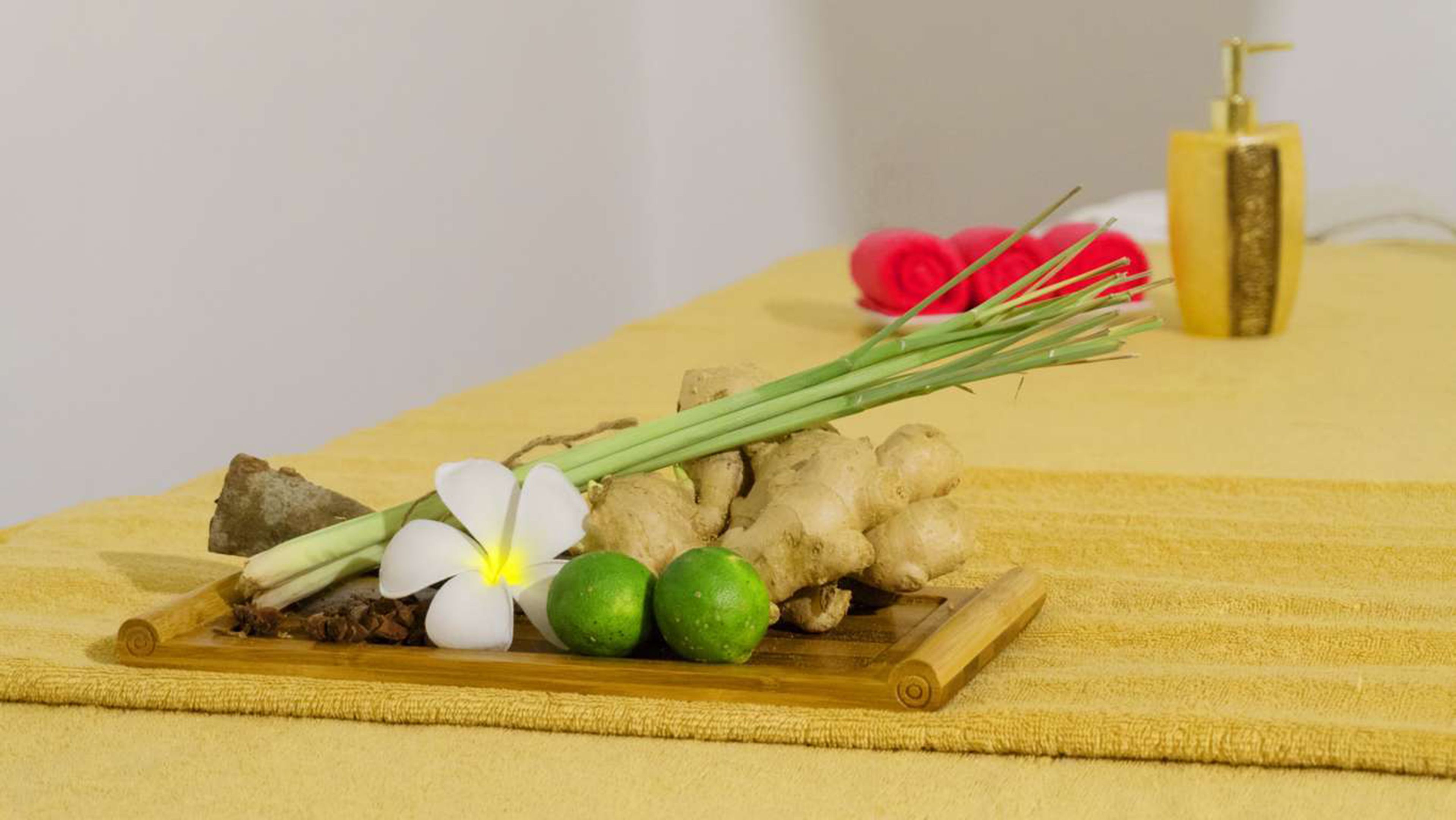 Una bandeja con jengibre, lima, una flor blanca y cebolletas sobre una toalla amarilla.
