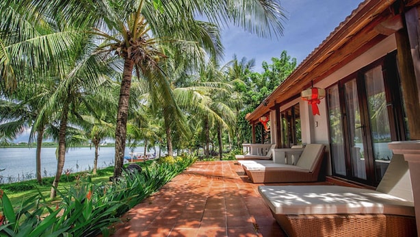 A covered outdoor seating area with a view of the water and palm trees. - Vinh Hung Riverside Resort & Spa (Da Nang)