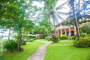 A lush garden with a stone pathway leading to a building with a balcony.