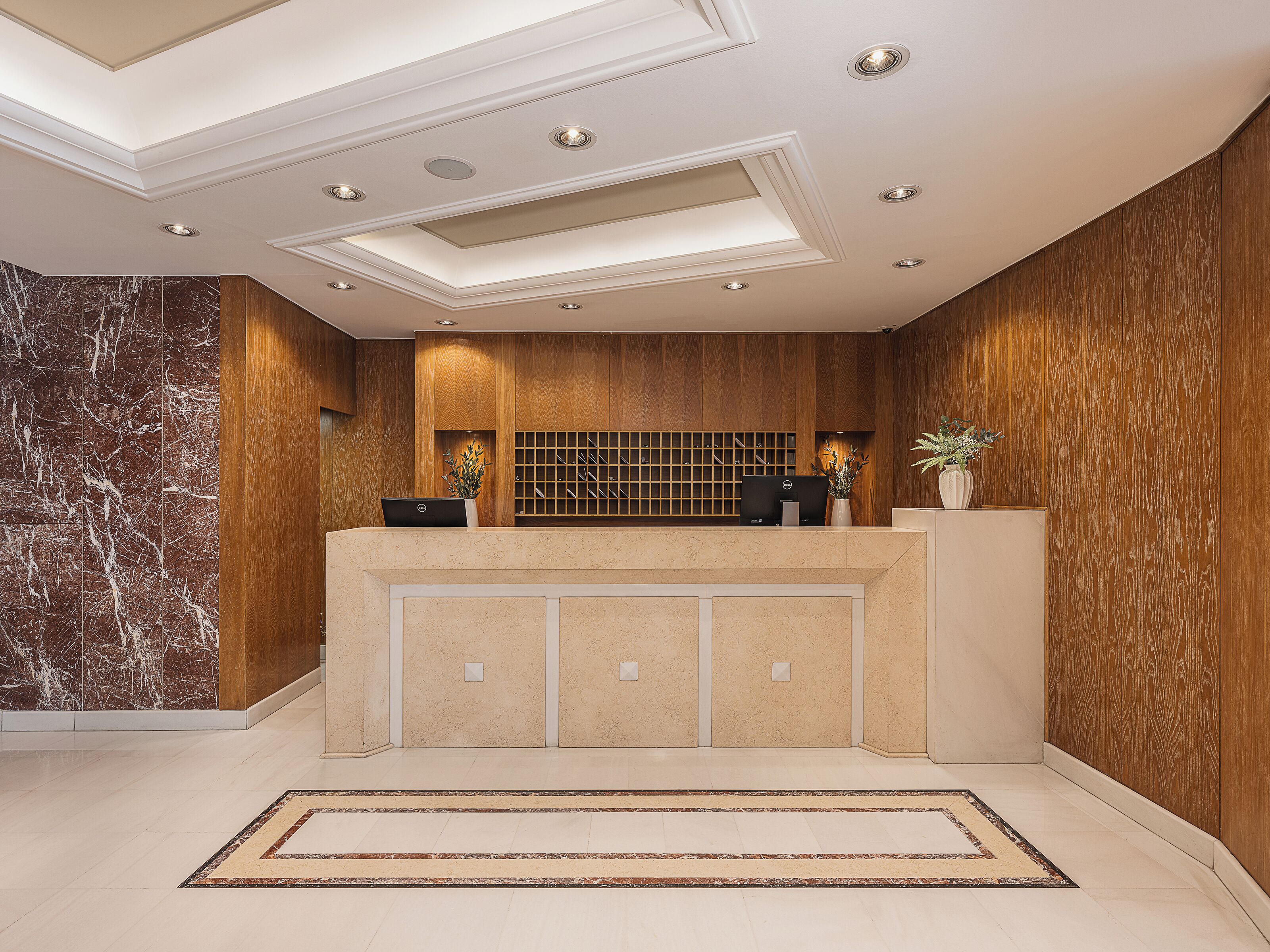 A reception area with a marble wall, wooden paneling, a reception desk, and a tiled floor.