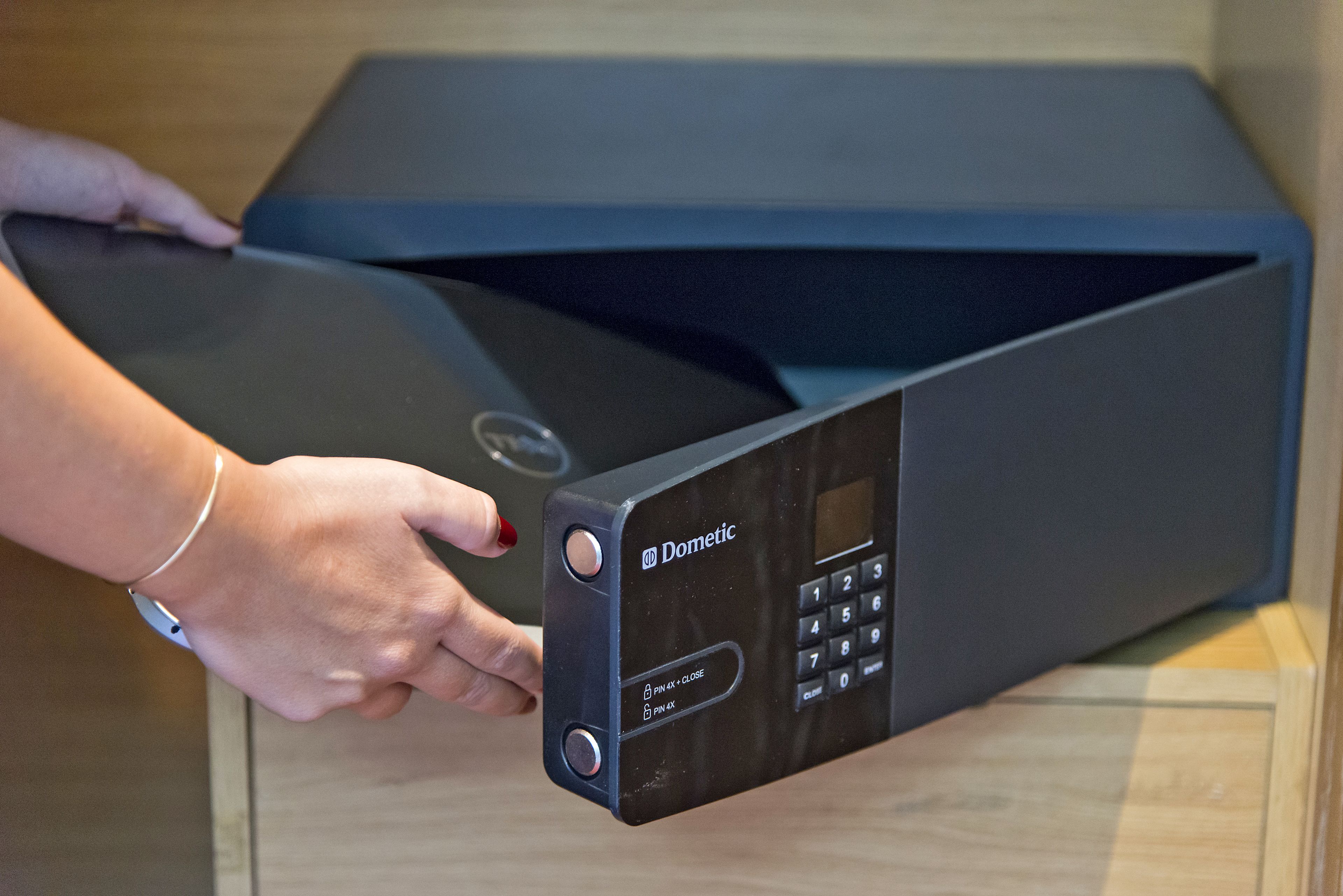 A black electronic device with a keypad and a display screen, held by a person wearing a bracelet.