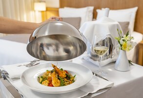 Una mesa de comedor con un plato de pasta de mariscos, una copa de vino blanco y un florero con flores.