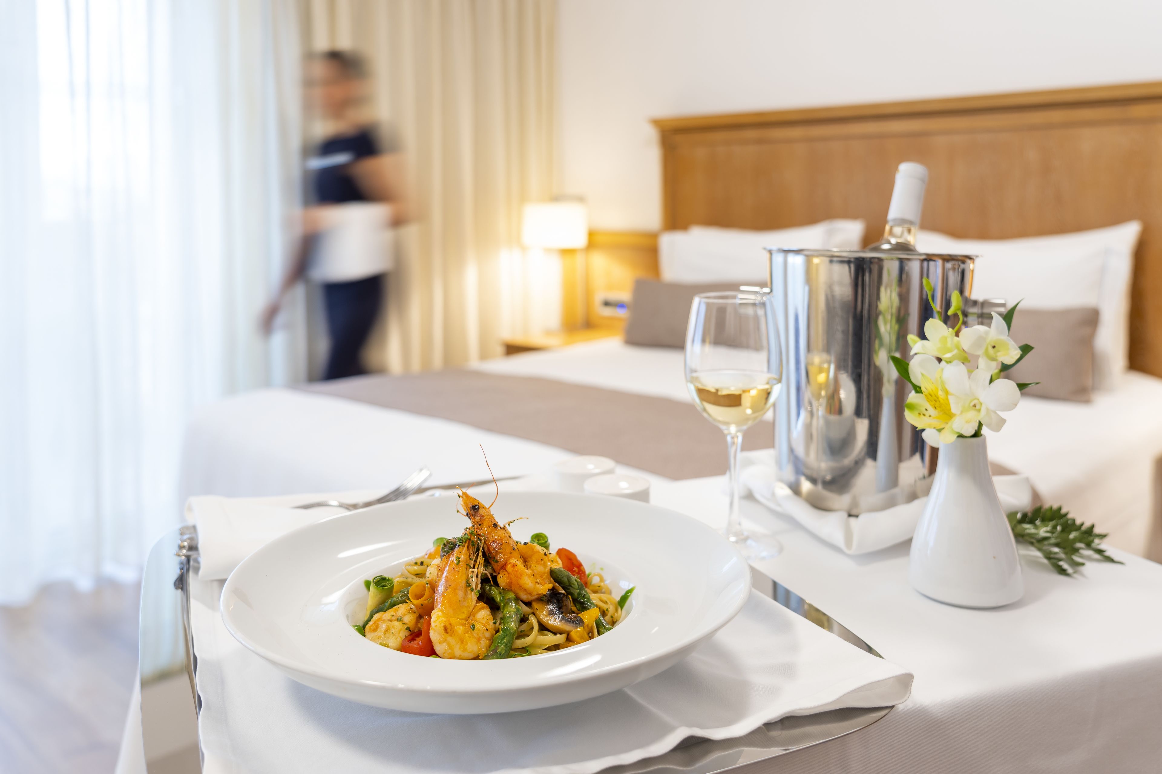A neatly arranged dining table with a seafood dish, a wine glass, and a decorative vase with flowers, set against a hotel room backdrop.