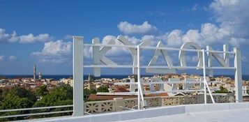 A white sign with the word "KIAON" against a backdrop of a coastal town with buildings and a clear sky.