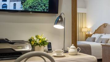 Una camera d'albergo con un letto, comodino con lampada, televisore a parete e vista su un edificio e spazi verdi.