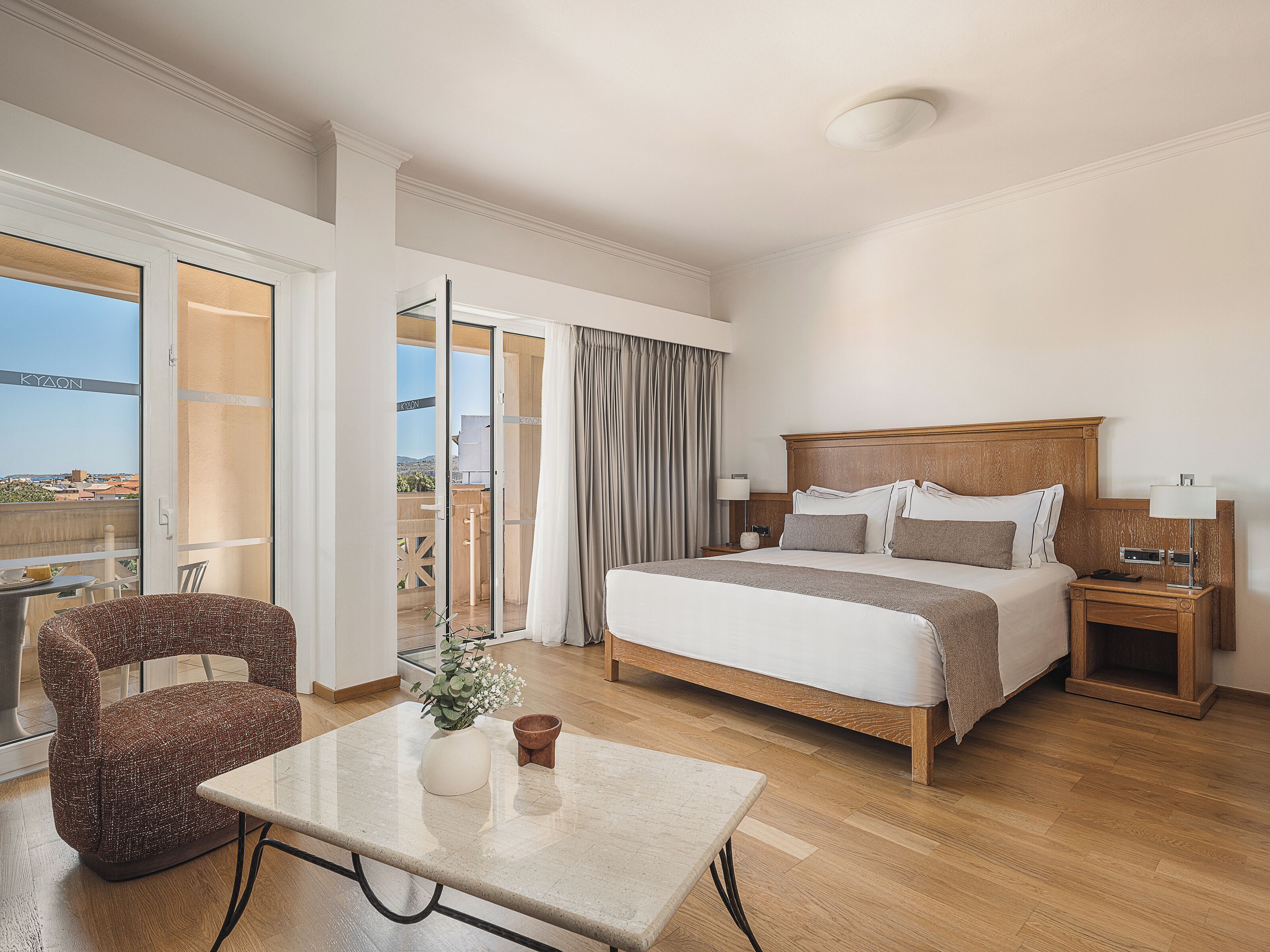 A hotel room with a bed, bedside table, chair, and a view of the outdoors.