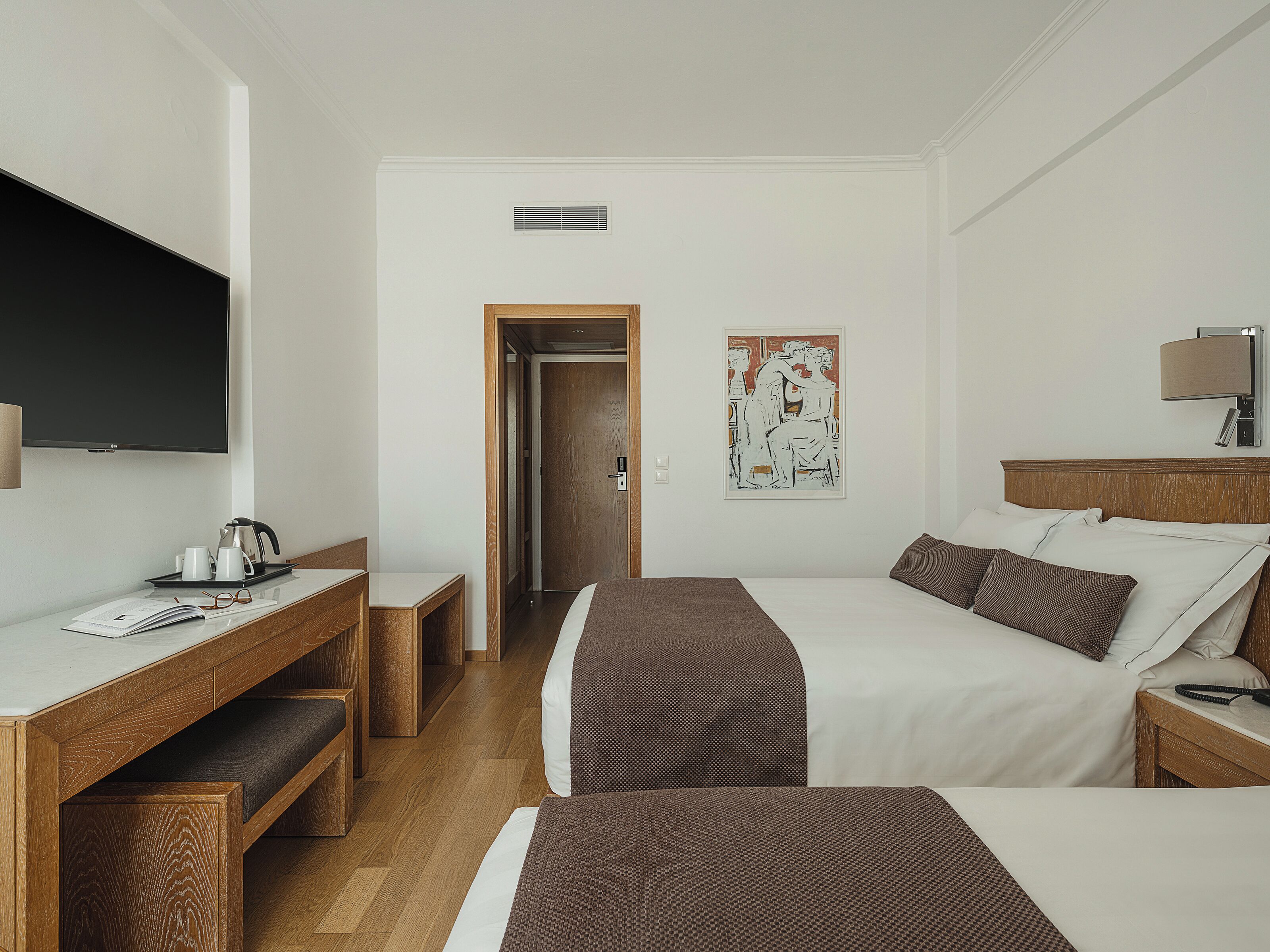 Une chambre d’hôtel comprenant un lit, une table de chevet, un bureau avec une chaise, un téléviseur et un tableau au mur.
