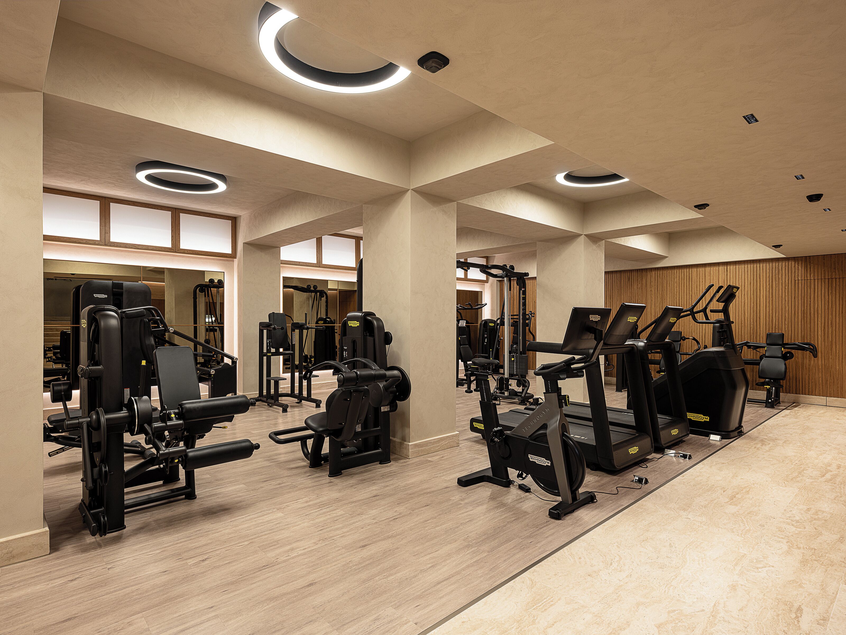 Ett modernt gym med olika typer av träningsutrustning, inklusive löpband och styrketräningsmaskiner, och med infälld belysning.