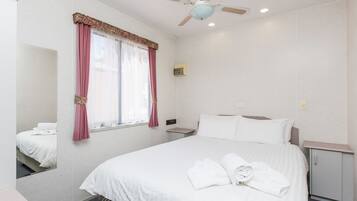 A hotel room with a bed, a nightstand, a mirror, a ceiling fan, and a window with curtains.