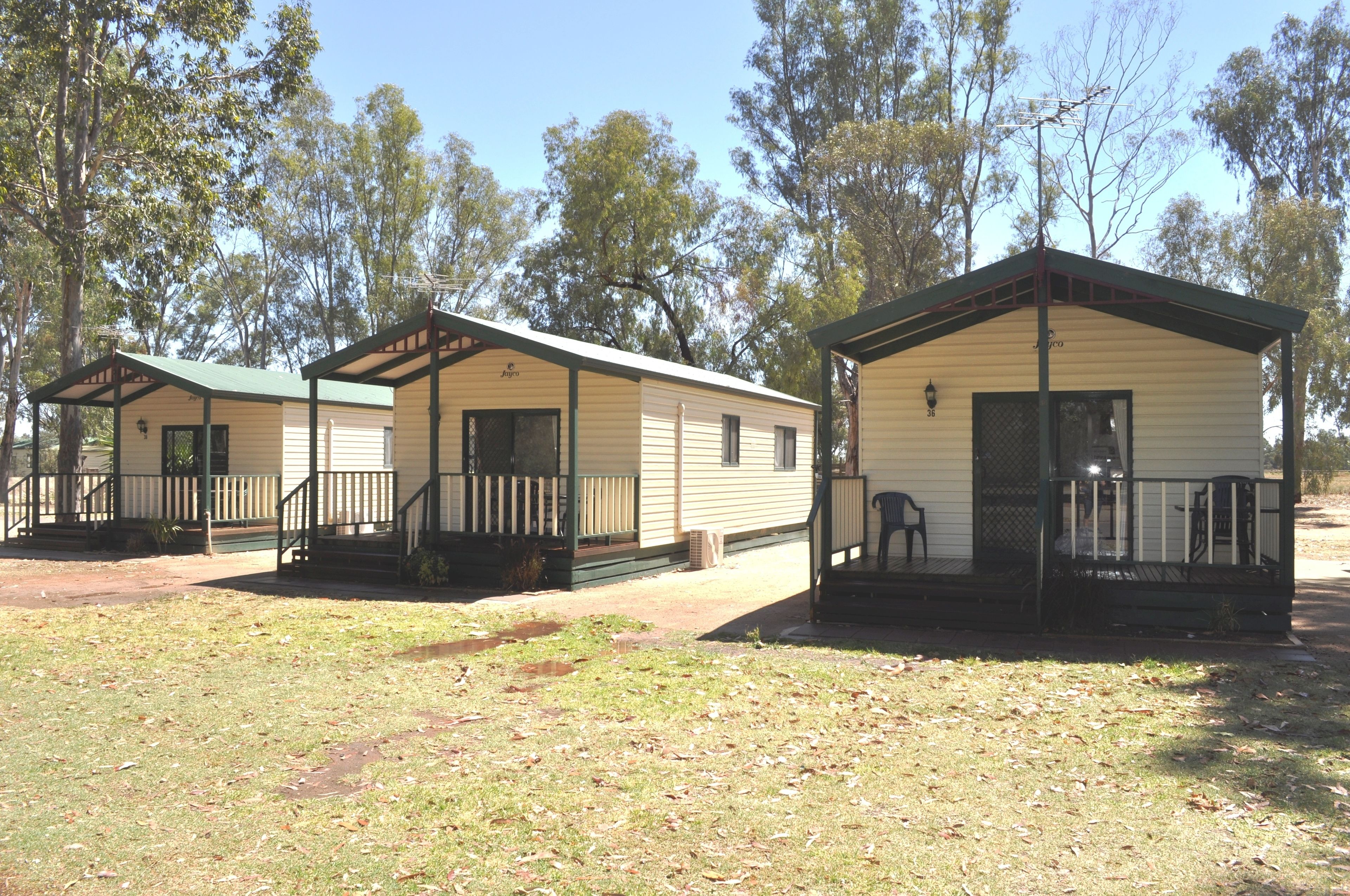 Three mobile homes with attached porches, each with a small porch chair and a lamp post.