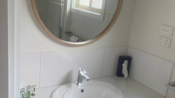 A bathroom with a round mirror, white sink, and wooden cabinets.