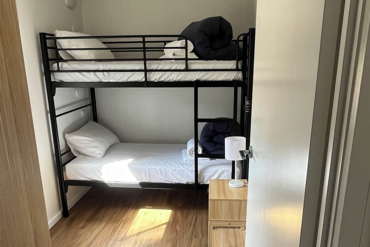 A bunk bed room with a wooden floor, a small wooden nightstand, and a white wall.