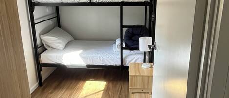Dormitorio con literas, piso de madera, mesita de noche de madera y pared blanca.