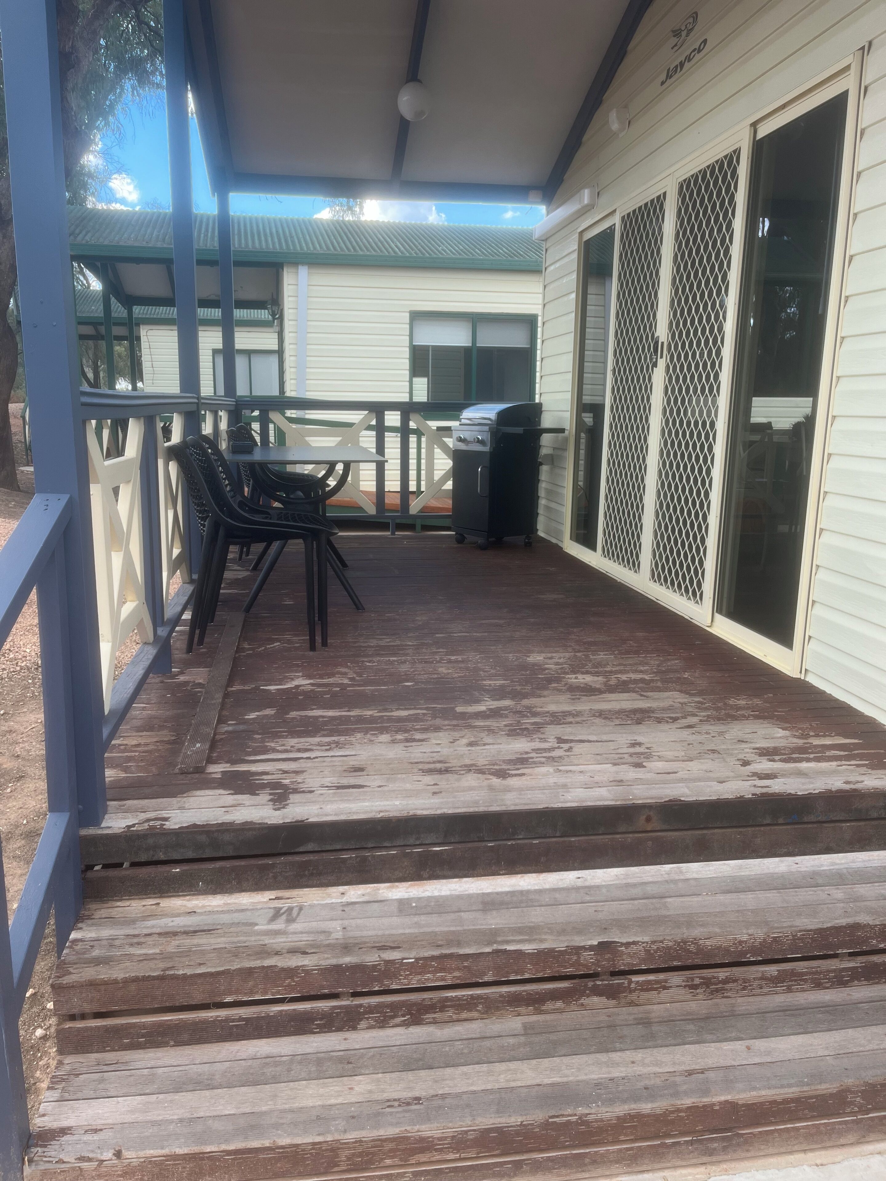 Un espacio exterior techado con una terraza de madera, una parrilla y una mesa con sillas.