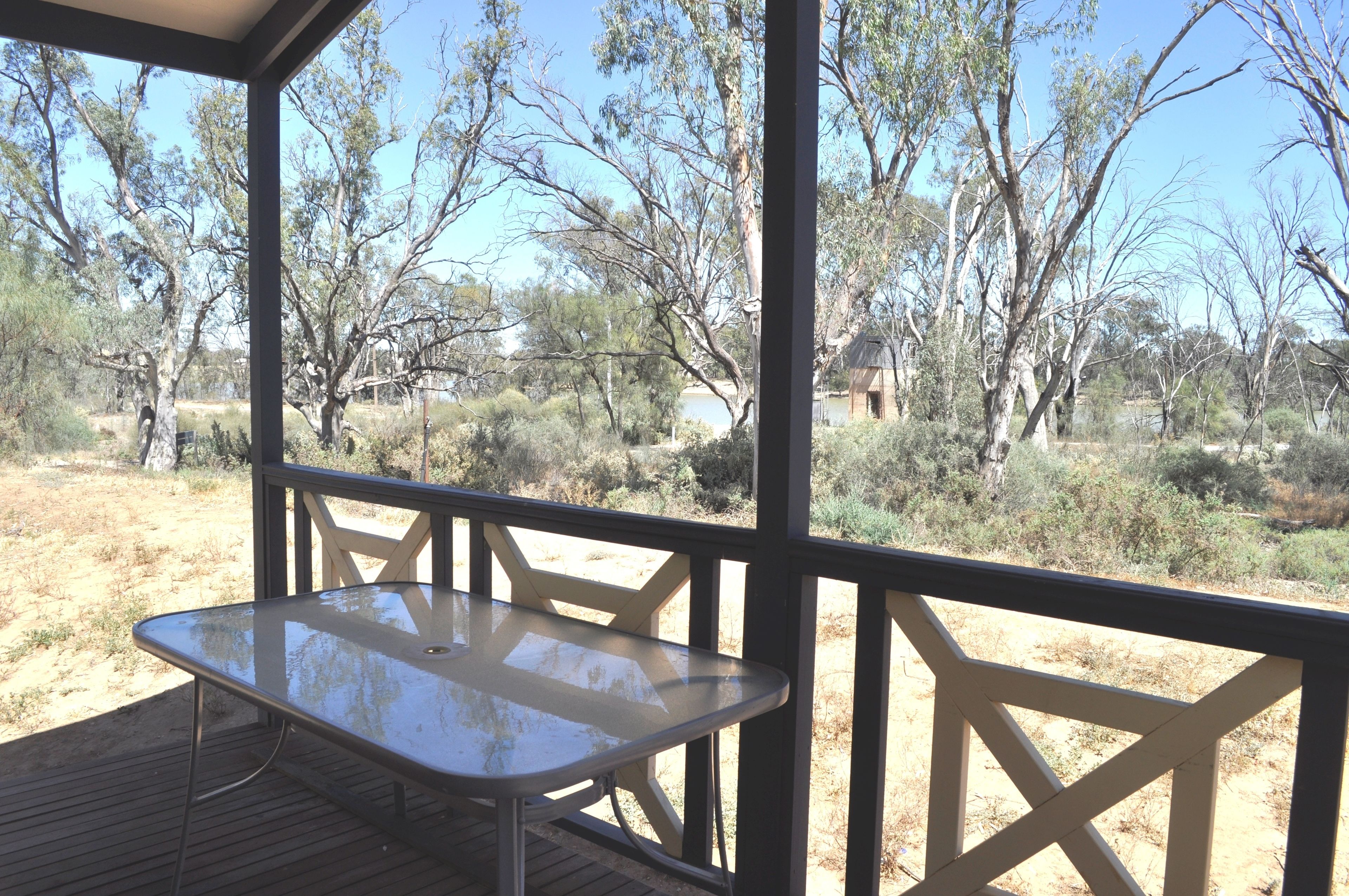 A covered outdoor area with a table and chairs, surrounded by trees and a dry landscape.