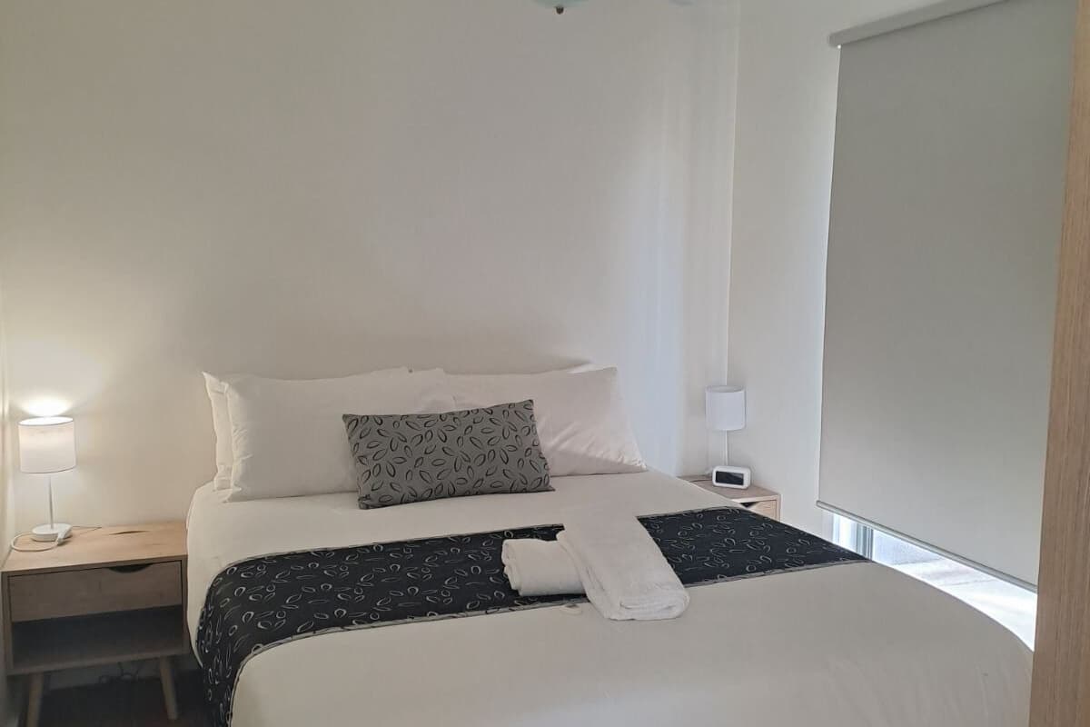 A modern bedroom with a bed, a ceiling fan, a bedside table with a lamp, and a window with a blind.