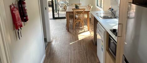 A modern kitchen with wooden flooring, a dining area with a table and chairs, and a refrigerator.