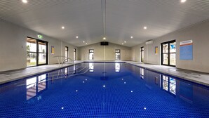An indoor swimming pool with clear ceiling lights, a tiled floor, and visible doors leading outside. - Discovery Parks - Geelong (Belmont)