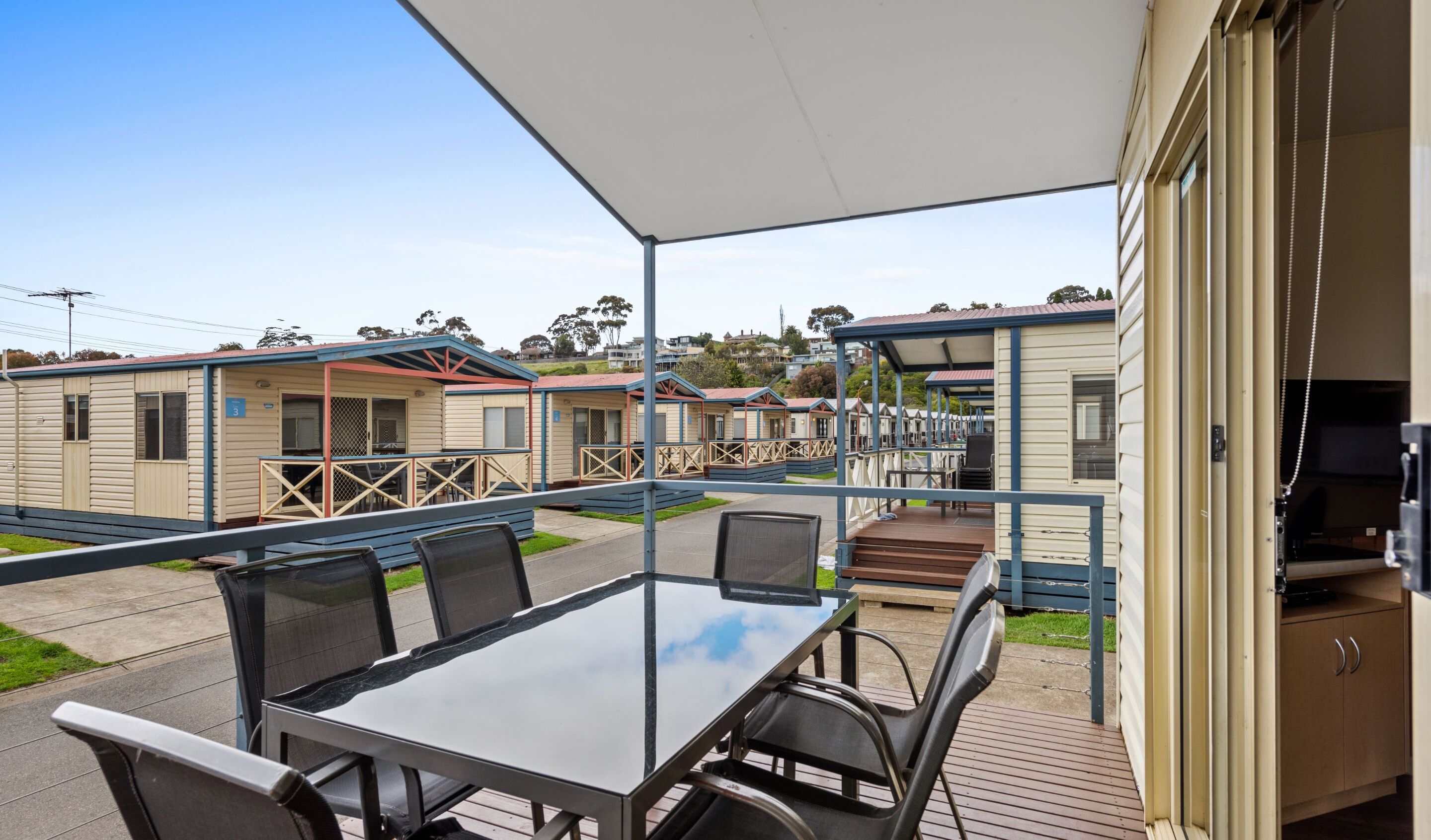 Un espace extérieur abrité, équipé d’une table et de chaises, d’un barbecue, et offrant une vue sur des mobil-homes au loin.