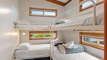 A bunk room with three beds, each with a window, and a small table with a lamp.