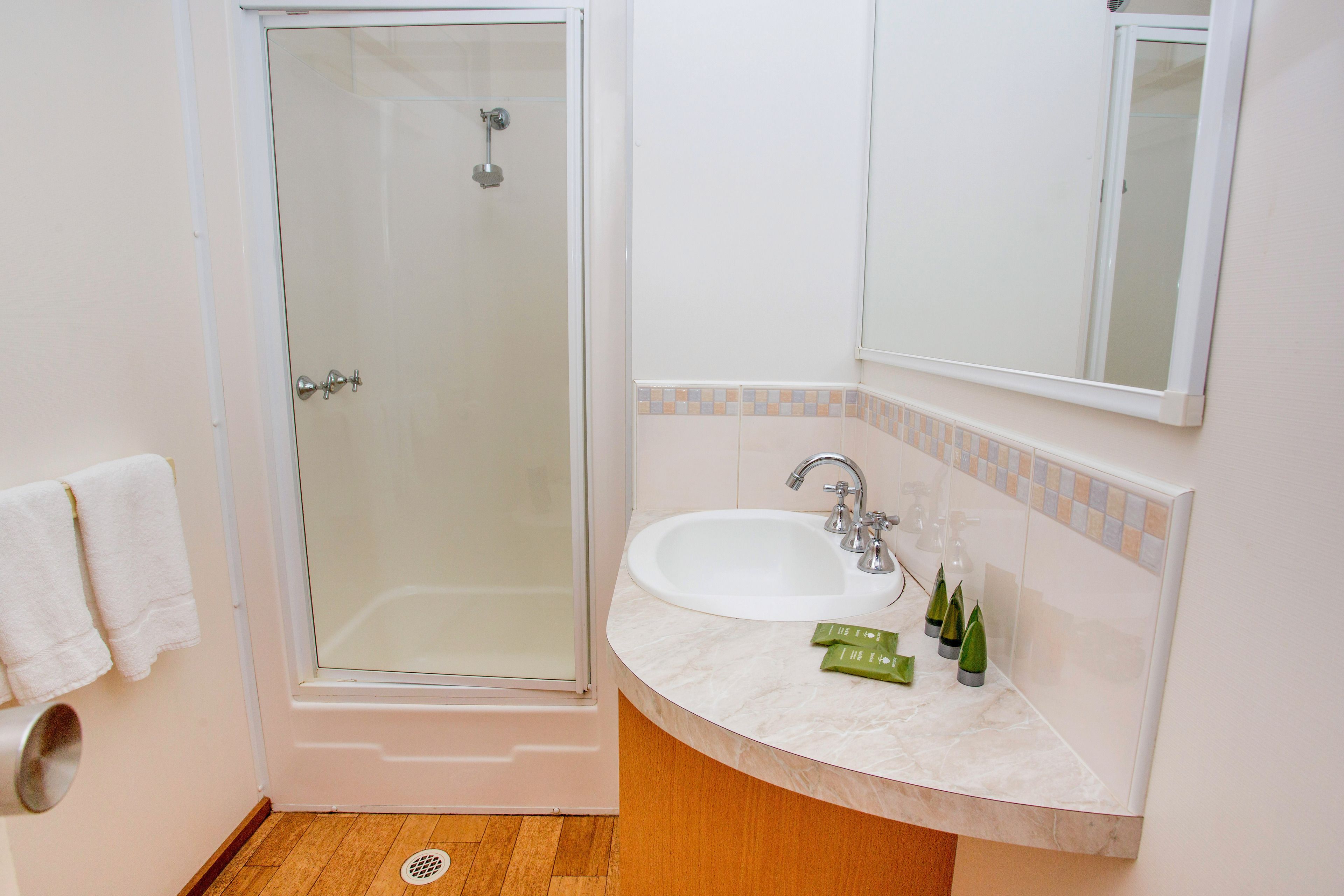 Un baño con ducha de vidrio, un lavamanos blanco y un espejo encima.