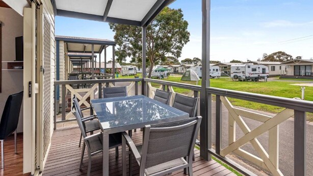 A covered outdoor area with a glass table and chairs, overlooking a caravan park. - Discovery Parks - Geelong (Belmont)