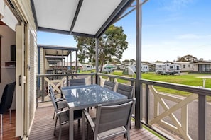 A covered outdoor area with a glass table and chairs, overlooking a caravan park. - Discovery Parks - Geelong (Belmont)