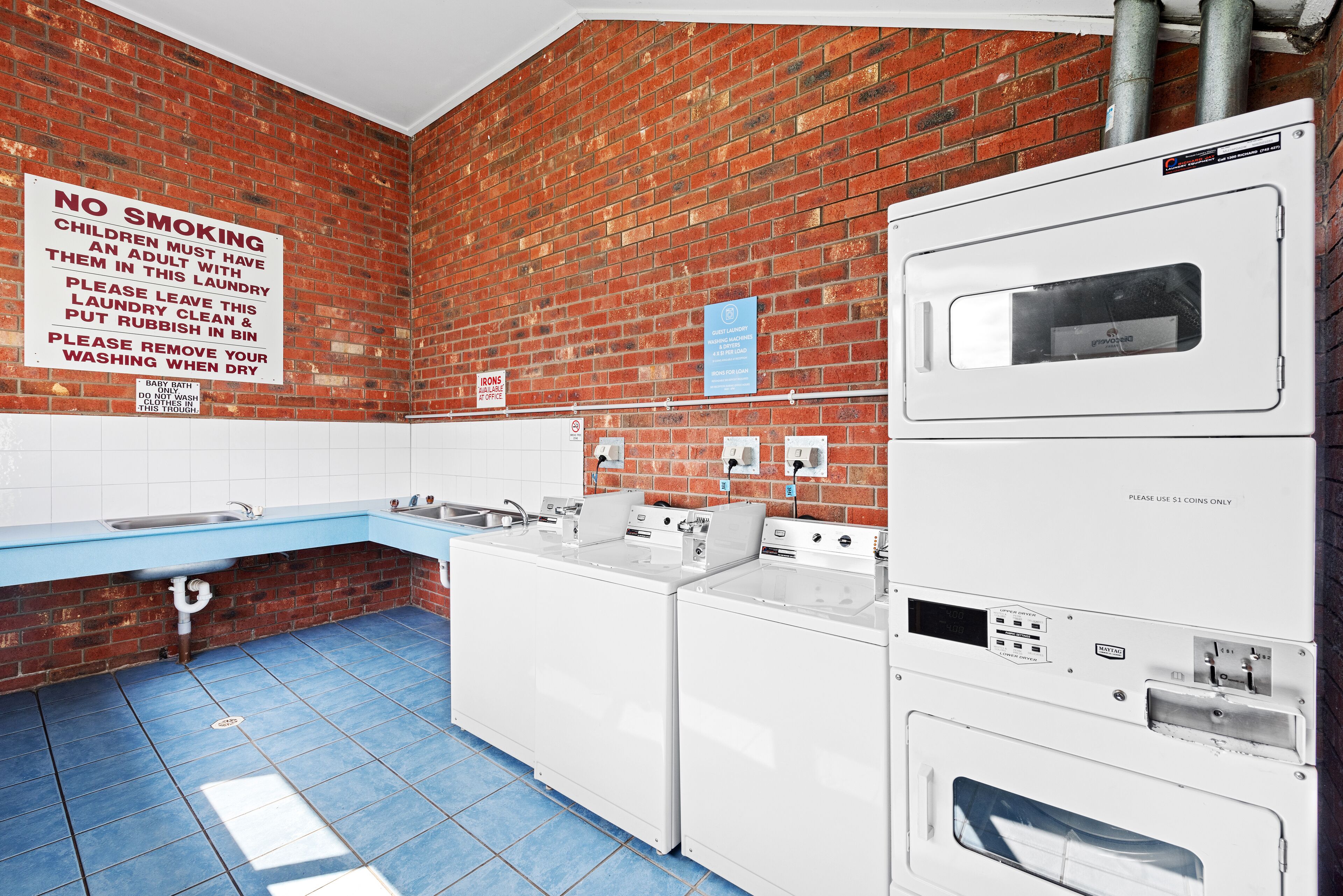 A laundry room with a brick wall, a sink, and two washing machines.