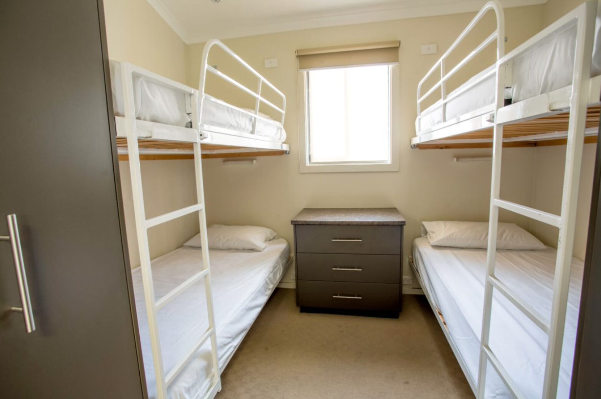 A small, compact room with bunk beds, a dresser, and a window.
