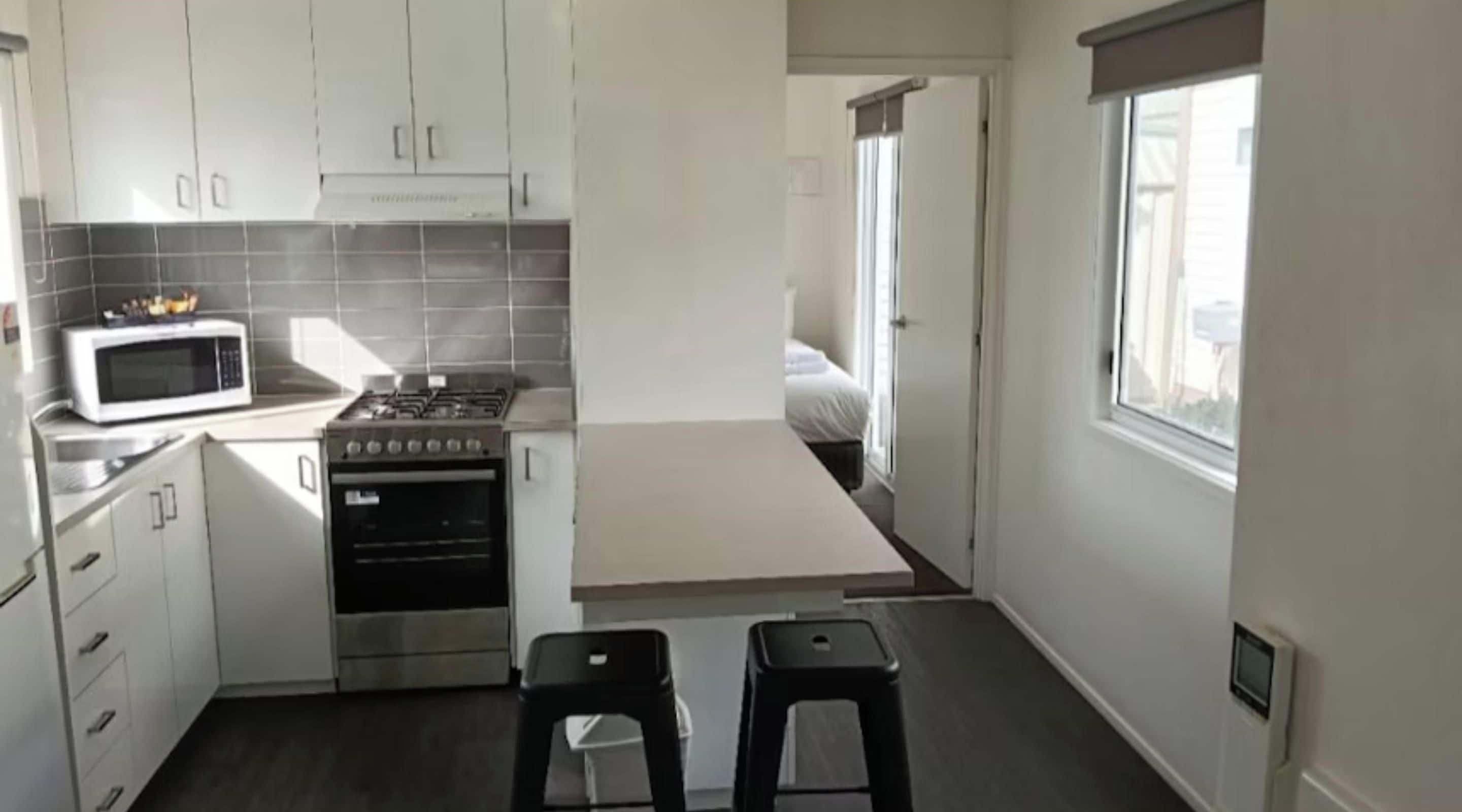 A compact kitchen with white cabinets, a microwave, a stove, and a small dining area with stools.